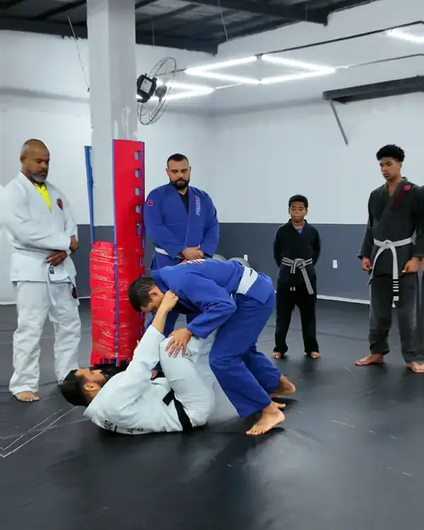 Alunos treinando em duplas no tatame, com o professor acompanhando