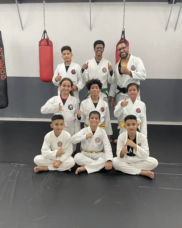 Turma Kids de kimono, sentada no tatame com o professor